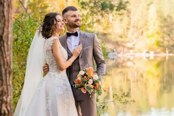 Młoda para w otoczeniu jesiennej przyrody. Ona w sukni ślubnej, on w garniturze. Trzymają bukiet. Zmieniła panieńskie nazwisko.