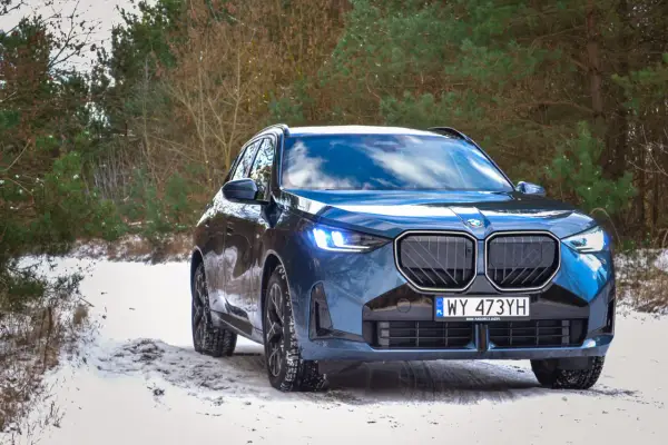 Niebieskie, nowe BMW X3 na ośnieżonej drodze w lesie. Zimowe opony gotowe na wyzwania.