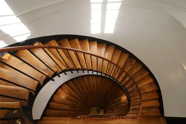 Vue plongeante d'un escalier en colimaçon en bois, parfait pour une rénovation cage escalier immeuble. La lumière naturelle illumine les marches.