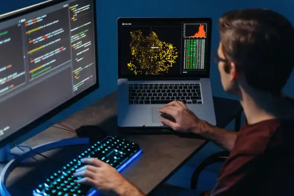 Młody big data engineer analizuje dane na ekranach, tworząc wizualizacje i pisząc kod.