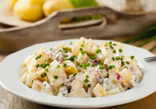 Pyszna, oryginalna kartoffelsalat z ziemniaków, ogórków kiszonych i cebuli, posypana szczypiorkiem.