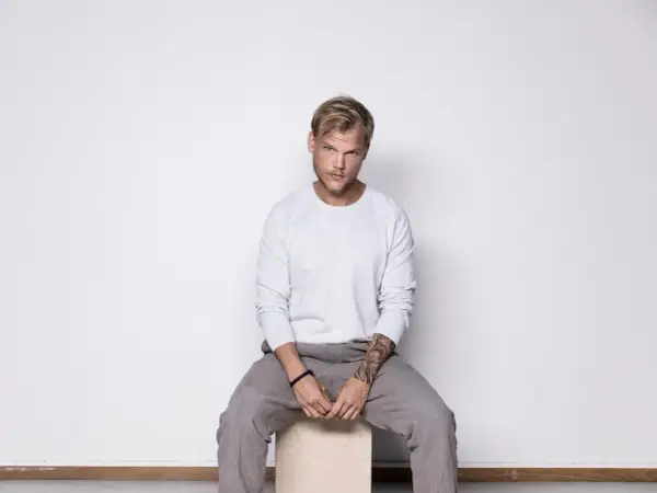 Avicii, siedzący na stołku, w szarym swetrze i spodniach. Jego śmierć wciąż budzi pytania.