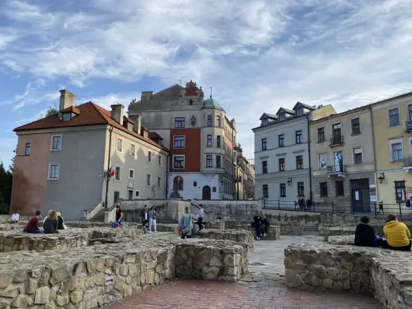 Ruiny zamku w Lublinie z ludźmi odpoczywającymi na kamiennych murach i zabytkowymi kamienicami w tle.