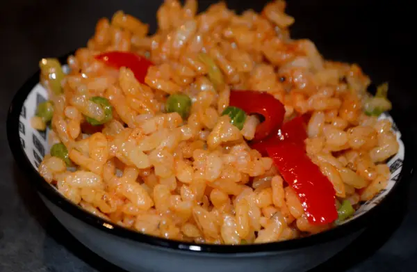 Un bol de riz coloré avec des petits pois et des poivrons rouges, parfait pour une recette salade riz facile et rapide.