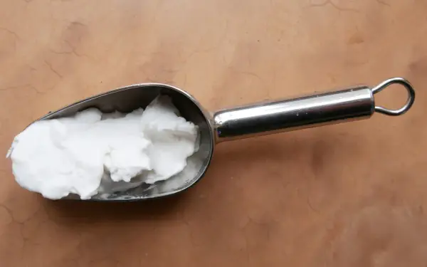 Une cuillère métallique contient une pâte blanche, peut-être de la cire saponifiée sur enduit chaux, prête à être appliquée.