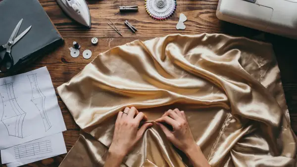 Manos ajustando tela dorada, lista para un diseño con punto jacquard. Patrones, tijeras y máquina de coser a la vista.