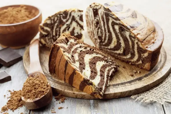 Wilgotne ciasto zebra z czekoladowymi i waniliowymi pasami, pokrojone na plastry, obok kakao i czekolady.