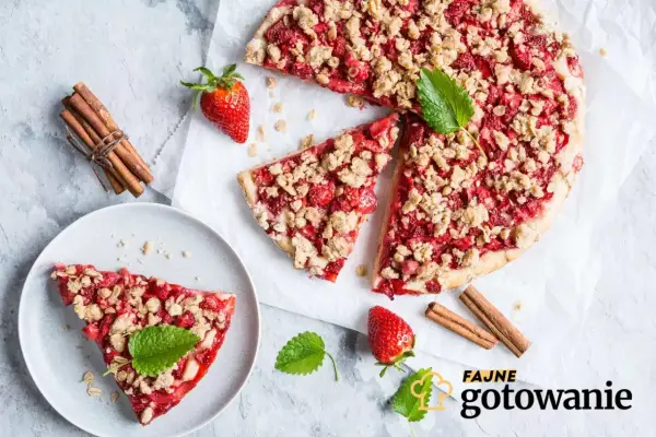 Pyszna tarta z truskawkami i kruszonką, udekorowana miętą, obok laski cynamonu i świeżych truskawek.
