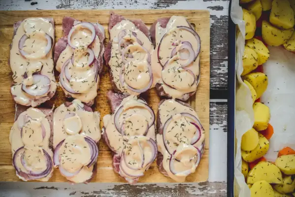 Schab pieczony w plastrach, polany kremowym sosem i posypany ziołami, obok pieczone ziemniaki.