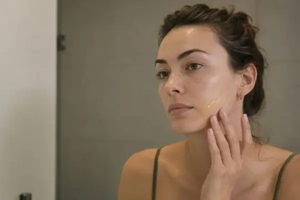 Kobieta aplikuje serum na twarz, zastanawiając się, czym są retinoidy i jak mogą poprawić jej cerę.