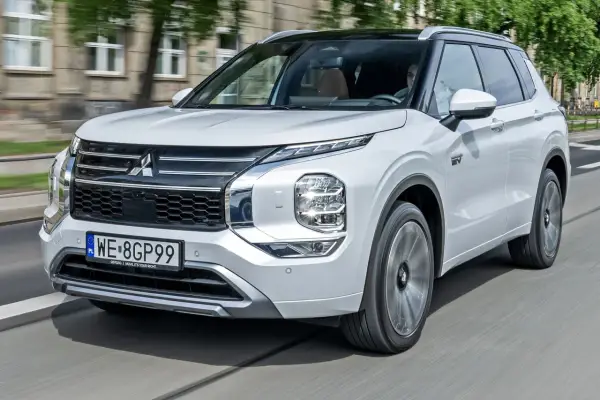 Biały Mitsubishi Outlander PHEV, jeden z nowoczesnych modeli tej marki, jedzie po mieście.
