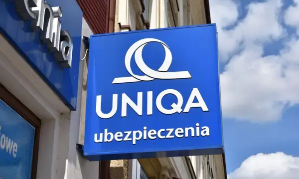 Niebieski szyld z logo i napisem "UNIQA ubezpieczenia". Firma UNIQA oferuje ubezpieczenia.