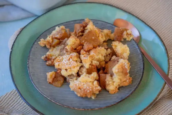 Ein Teller mit warmem Apfel Crumble, bestäubt mit Puderzucker. Die goldbraunen Apfelstücke und knusprigen Streusel laden zum Genießen ein.
