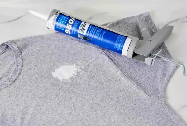 Zaschnięty silikon na szarym T-shircie i pistolet do jego aplikacji. Dowiedz się, jak usunąć zaschnięty silikon z ubrania.