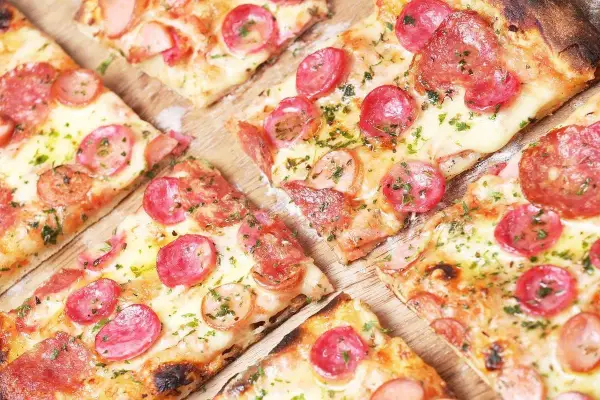 Kawałki pysznej pizzy cienkie ciasto z kiełbasą i serem, posypane ziołami. Idealna na szybką przekąskę.