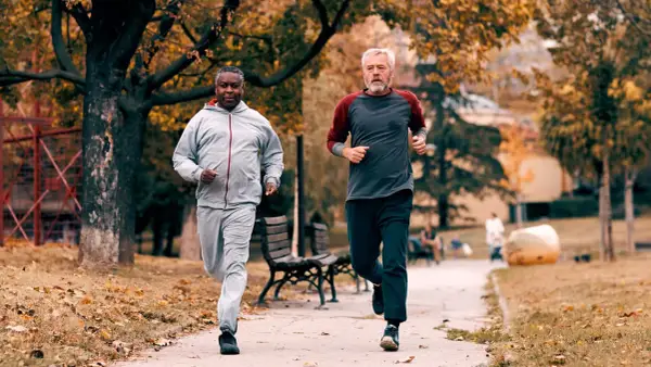 Zwei Männer im Herbstpark trainieren für den Halbmarathon. Sie laufen auf einem Weg, umgeben von bunten Blättern.