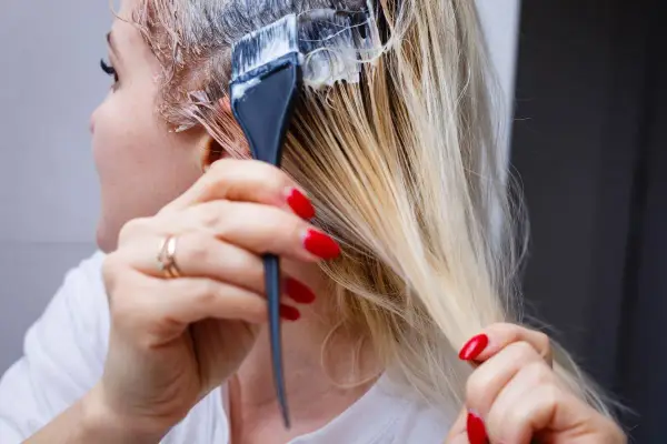 Application d'une patine sur des cheveux blonds. Le dosage précis est essentiel pour obtenir la teinte désirée.