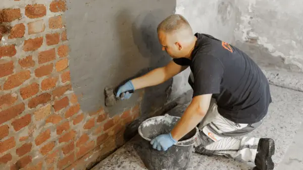 Mann verputzt Ziegelwand im Keller, um muffigen Geruch im Keller mit Hausmittel zu bekämpfen.