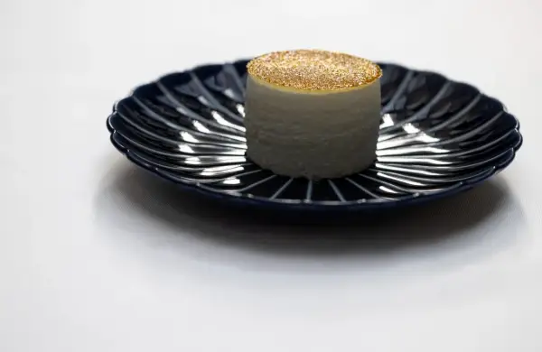 Un cylindre blanc, saupoudré d'or, sur une assiette bleue. Une idée de quoi manger à Paris pour une expérience culinaire unique.