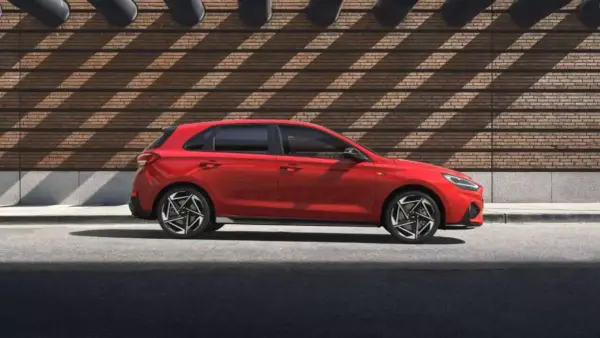 Czerwony Hyundai i30 stoi na tle ceglanej ściany z ciekawymi cieniami.
