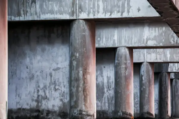 Columnas y vigas de concreto con textura desgastada, creando un patrón rítmico bajo la luz.