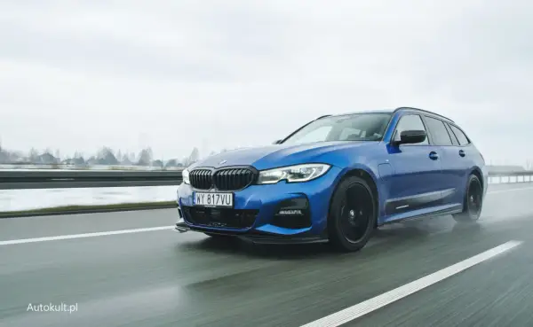 Niebieskie BMW 330e na mokrej drodze, z widocznymi kroplami deszczu na karoserii.