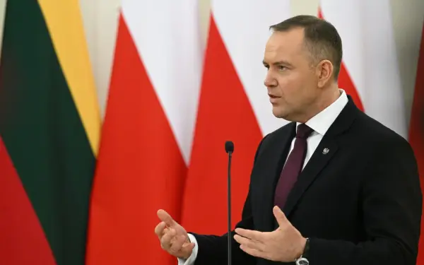 Karol Nawrocki, w garniturze, przemawia na tle flag. Jego gestykulacja i pewność siebie mogą być powodem, dlaczego Karol Nawrocki stał się nowym liderem sondaży zaufania na prawicy.