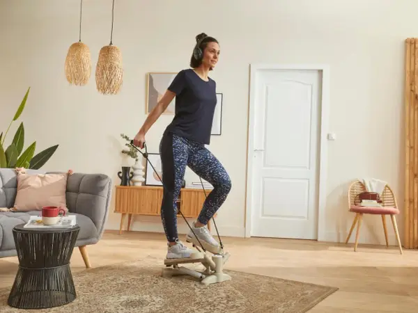 Une femme fait du step à la maison, casque sur les oreilles, pour un entraînement cardio efficace dans son salon.