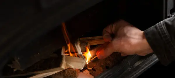 Main allumant un feu dans un poêle à bois avec une allumette.