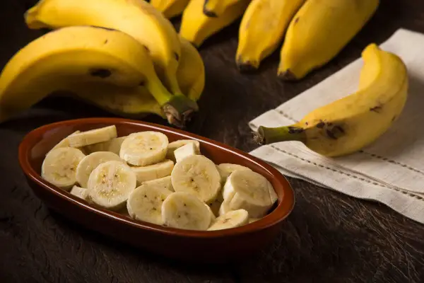 Kawałki banana w misce i cały banan obok. Pomyśl o tym, ile energii dostarcza jeden banan, kalorie to tylko jedna z jego zalet.