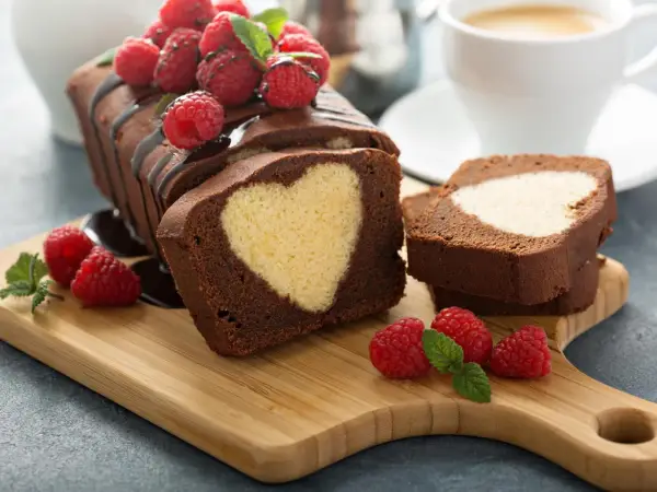 Schokoladen-Kastenkuchen mit einem hellen Herz im Inneren, garniert mit frischen Himbeeren und Schokoladensauce.
