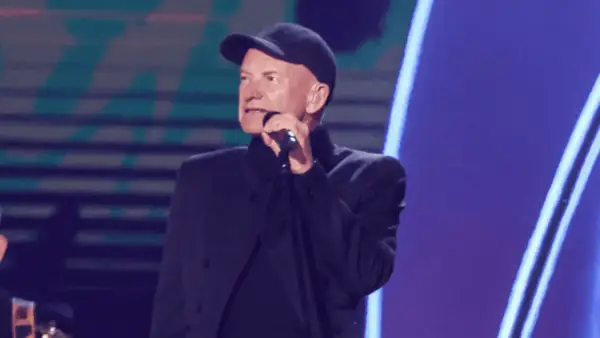 Sting w czapce i czarnym stroju śpiewa do mikrofonu. Ciekawe, ile Sting bierze za koncert, gdy występuje na tak dużej scenie.