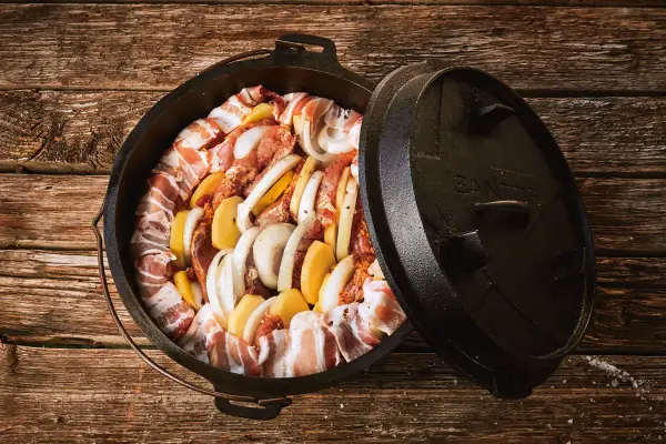 Dutch oven mit Fleisch, Kartoffeln und Zwiebeln, bereit für köstliche Dutch Oven Rezepte auf dem Gasgrill.