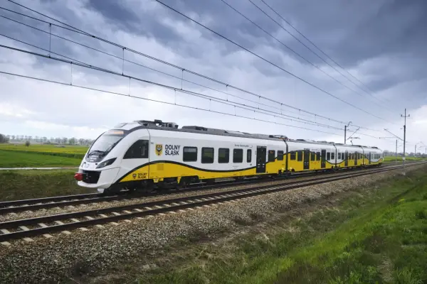 Pociąg Kolei Dolnośląskich z charakterystycznym żółto-białym malowaniem jedzie po torach. Zniżki dla żołnierzy zawodowych PKP to świetna okazja do podróżowania.