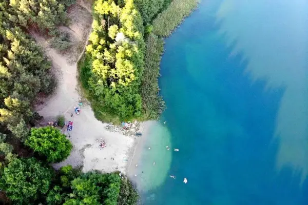 Plaża nad jeziorem tętni życiem. Ludzie odpoczywają na piasku, kąpią się w krystalicznie czystej wodzie, ciesząc się letnim dniem.