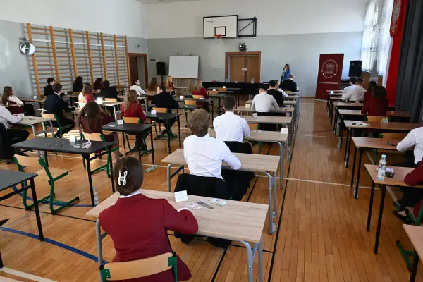 Uczniowie siedzą w ławkach, skupieni na pisaniu egzaminu. To ważny moment, przygotowanie do lektury na maturę.