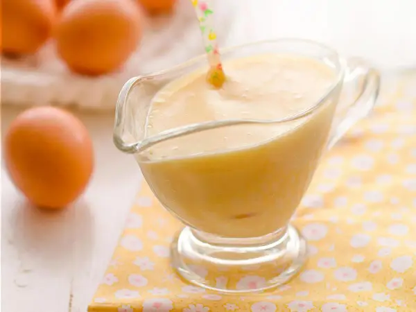 Crema pastelera cremosa en una salsera de cristal, con huevos frescos al fondo. Perfecta para rellenar postres.