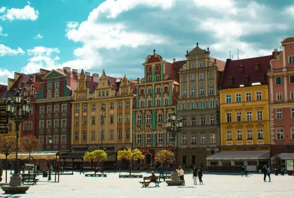 Kolorowe kamienice na starym rynku we Wrocławiu, z błękitnym niebem i białymi chmurami w tle.