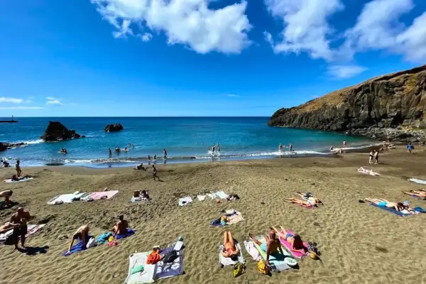Słoneczne madera plaże z turystami kąpiącymi się w turkusowym oceanie i opalającymi się na piasku.