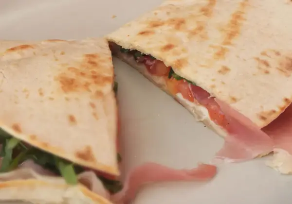 Pyszna piadina z szynką, pomidorami i rukolą, złożona na pół, prezentuje apetyczny przekrój.