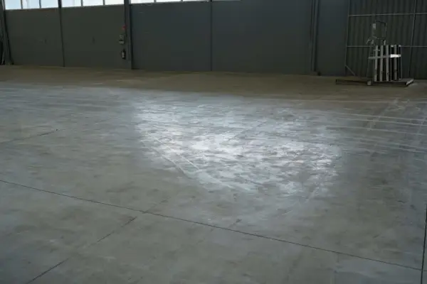Vaste entrepôt avec une dalle béton qui part en poussière, marquée par des traces de passage.