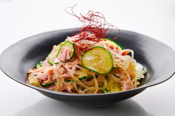 A refreshing harusame salad with glass noodles, sliced cucumber, and ham, garnished with delicate red chili threads.