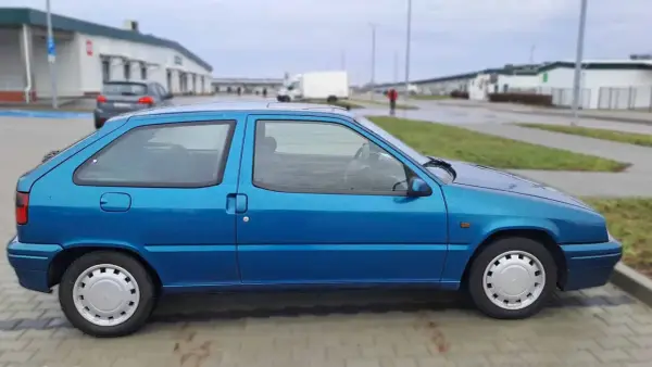 Niebieski Citroen ZX stoi na parkingu. W tle widać budynki i białą ciężarówkę.