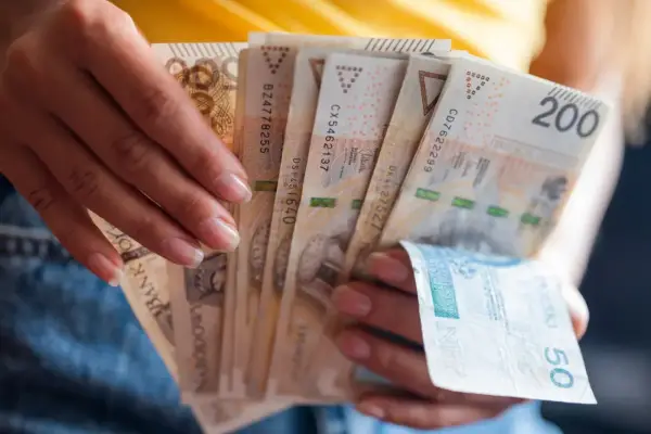 Dłonie trzymają plik banknotów 200 zł i 50 zł. Jak egzekwować obowiązek naprawienia szkody, gdy sprawca nie chce zapłacić?