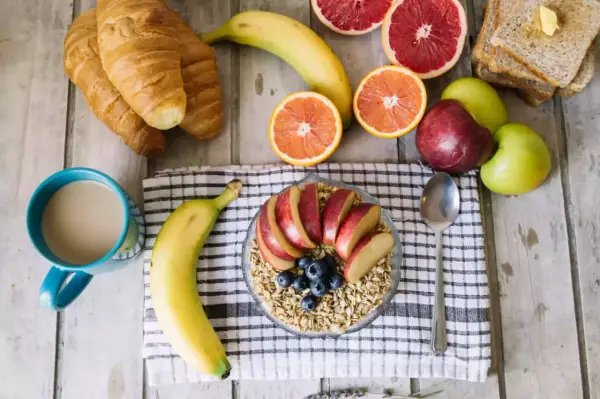 Pyszne i lekkostrawne śniadanie: owsianka z jabłkiem i jagodami, banan, croissanty, cytrusy i kawa.