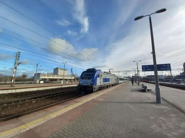 Pociąg na stacji, idealny środek transportu, by dowiedzieć się, jak dostać się do morza. Słońce i chmury na niebie.