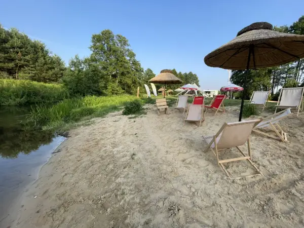 Plaża nad rzeką z leżakami i parasolami. W tle drzewa i niebo. Idealne miejsce na relaks, jak na konopnicy.