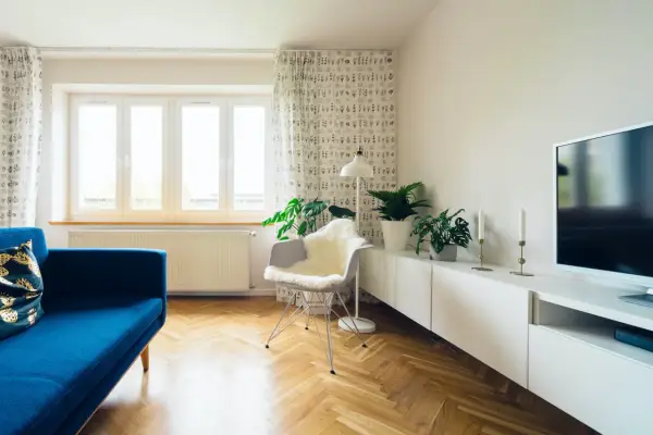 Jasny salon z niebieską kanapą i roślinami. Zasłony z wzorem pomogą jak wyciszyć pokój.