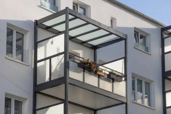 Nowoczesny balkon dostawny z przeszklonym zadaszeniem i balustradą, ozdobiony skrzynkami z kwiatami. Sprawdź balkon dostawny cena.