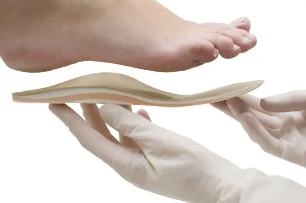 Une orthoplastie sur mesure est présentée sous un pied, tenue par des mains gantées.